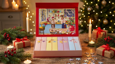 Puslespilskalender med juleillustration i åben gaveæske mellem grangrene og julelys