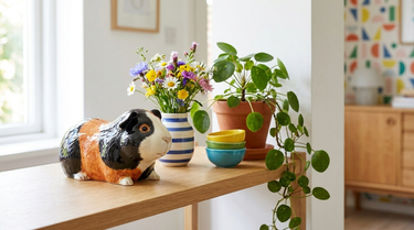 Sparegris formet som et marsvin i stentøj på en hylde med blomster og skåle